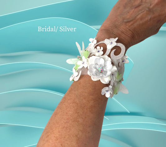 The Silver Bridal Bracelet- Lightweight faux suede magnetic bracelet w/ handmade satin/silk flowers with Silver Lame' flowers, and Austrian Crystal centers.. 2 Beautiful 3-D chiffon butterflies, Delicate white tulle, green silk and silvr Lame' leaves, scroll ribbon, silk and silver lame' flowers w/Austrian Crystal centers are the backdrop for this beautiful floral arm piece. $45.99