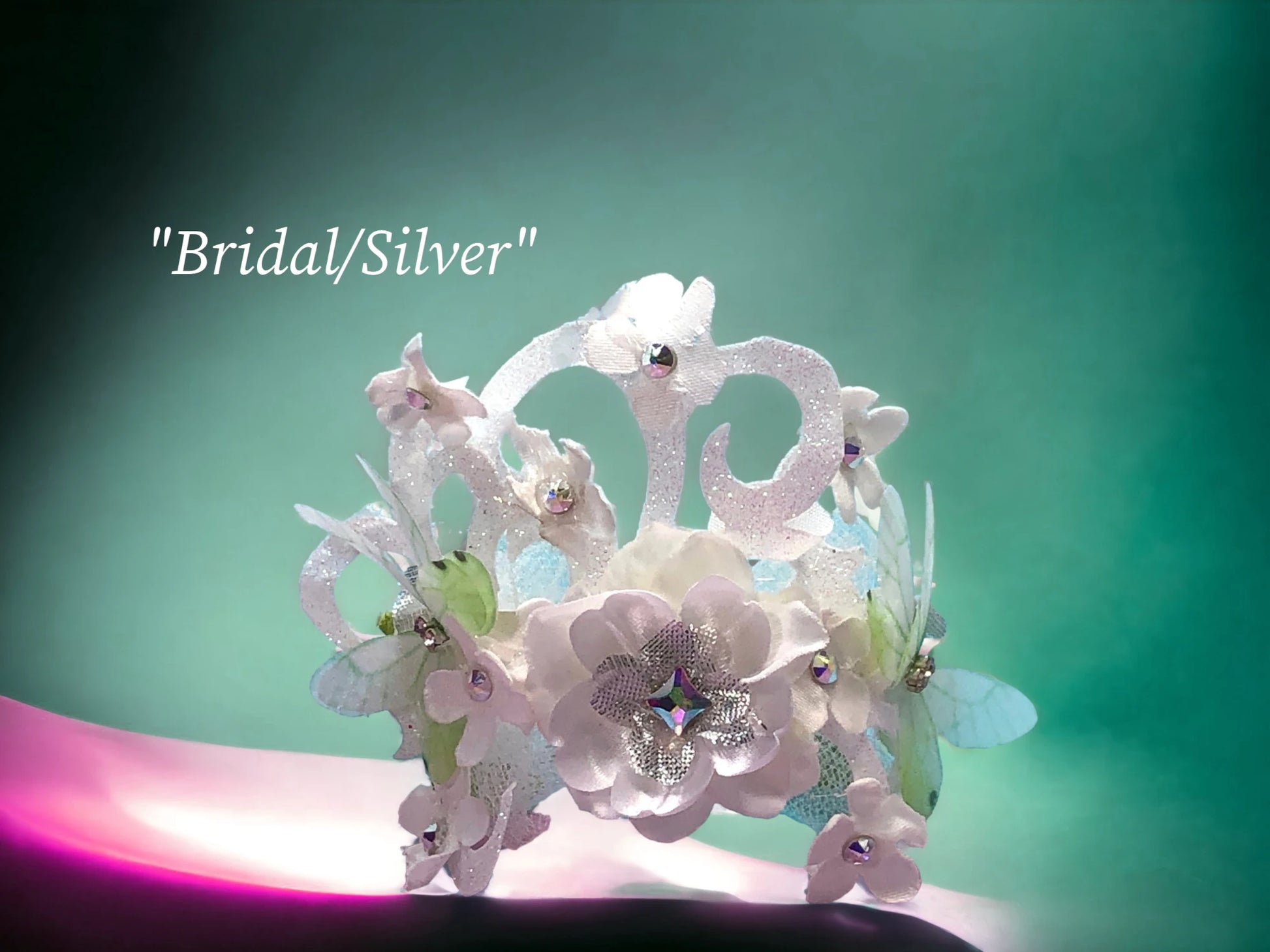 The Silver Bridal Bracelet- Lightweight faux suede magnetic bracelet w/ handmade satin/silk flowers with Silver Lame' flowers, and Austrian Crystal centers.. 2 Beautiful 3-D chiffon butterflies, Delicate white tulle, green silk and silvr Lame' leaves, scroll ribbon, silk and silver lame' flowers w/Austrian Crystal centers are the backdrop for this beautiful floral arm piece. $45.99