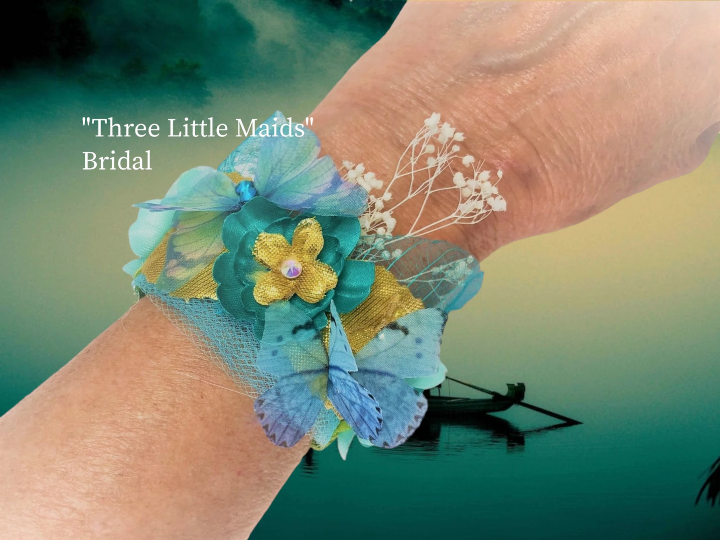 Three Little Maids-Lightweight magnetic closure bracelet w/ 3 contrasting Teal silk flowers and crystal centers. Green silk leaves, dried baby's breath, gold lame' leaves and flowers with crystal centers, Teal chiffon and crystal butterfly, Teal skeleton leaves, with crystal dew drops and delicate matching Tulle make up this wedding arm piece. $46.99